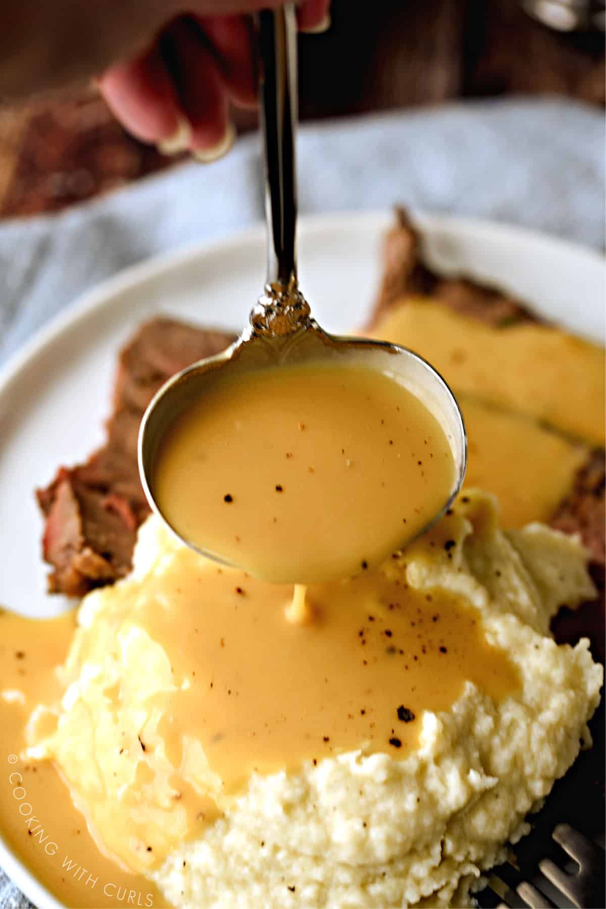 gravy being poured onto mashed cauliflower and slices of roast beef from a silver ladle.