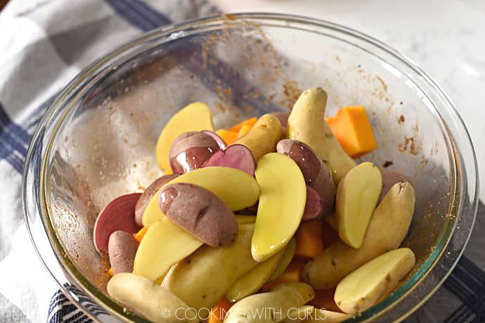 sliced fingerling potatoes and butternut squash cubes tossed with olive oil in a large glass bowl. 