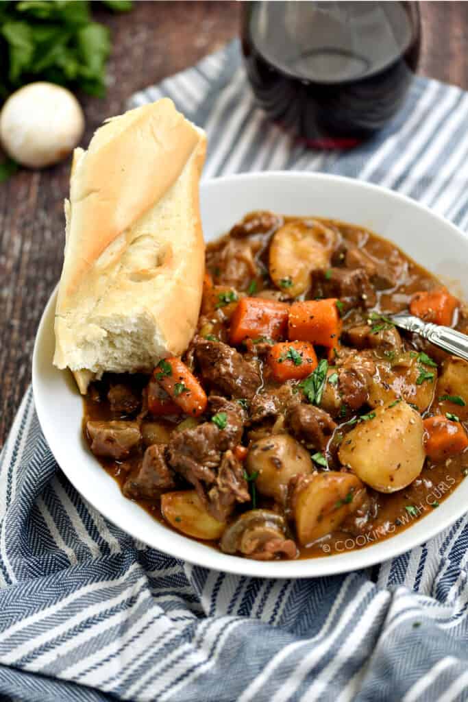 A big bowl of hearty, Instant Pot Beef Bourguignon served with a French baguette and red wine. 