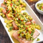 Four salmon filets topped with pineapple salsa on a white platter.