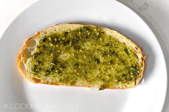 Basil pesto spread on a slice of bread sitting on a white plate.