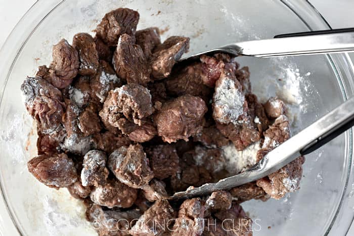 Beef chunks tossed with flour in a glass bowl. 