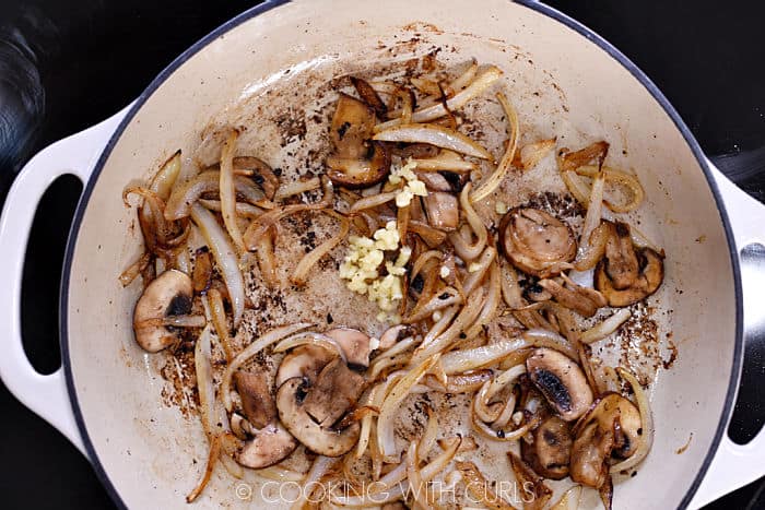 Browned onion slices, garlic and mushrooms in a skillet. 