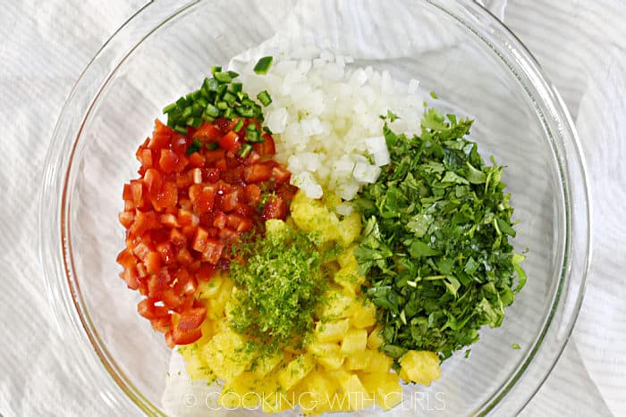 Chopped onion, pepper, pineapple, jalapeno, cilantro and lime zest in a glass bowl. 