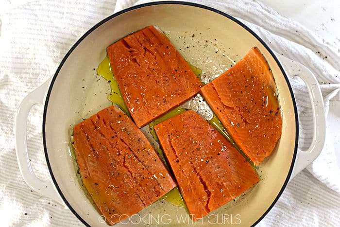 Four salmon filets drizzled with oil, salt and pepper in a white skillet. 