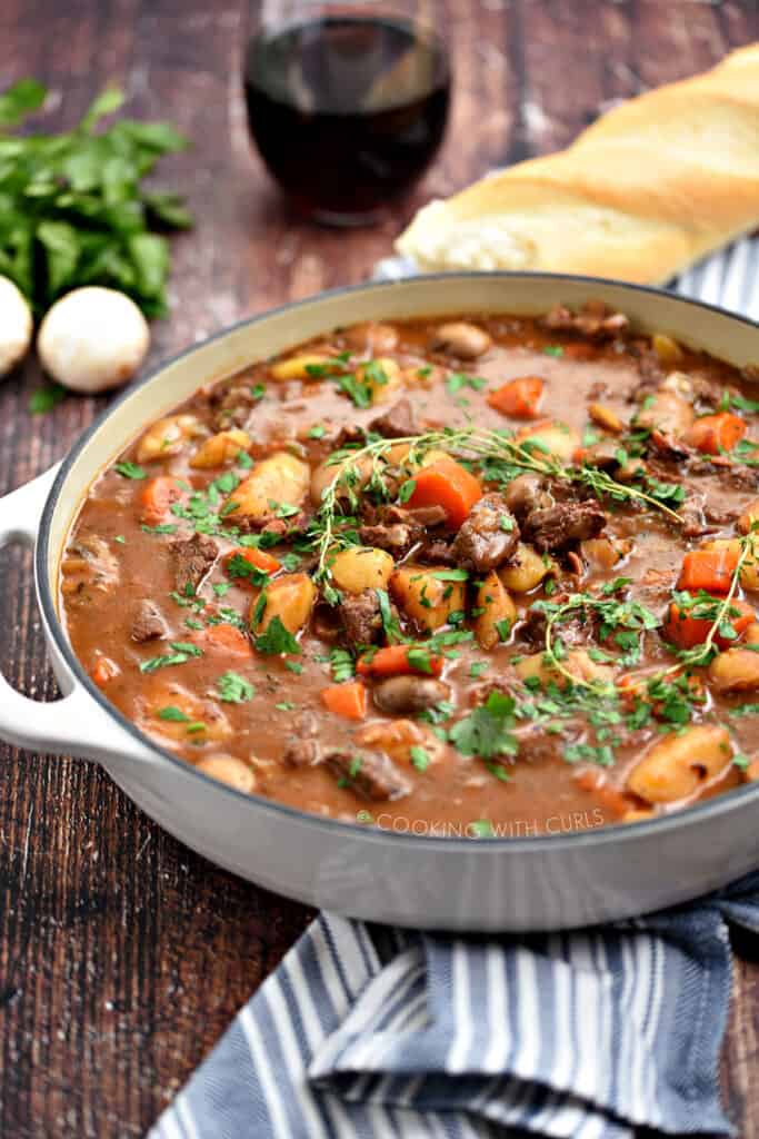 Cooked beef chunks, potatoes, mushrooms and carrots in a rich brown gravy topped with fresh thyme leaves in a white skillet.