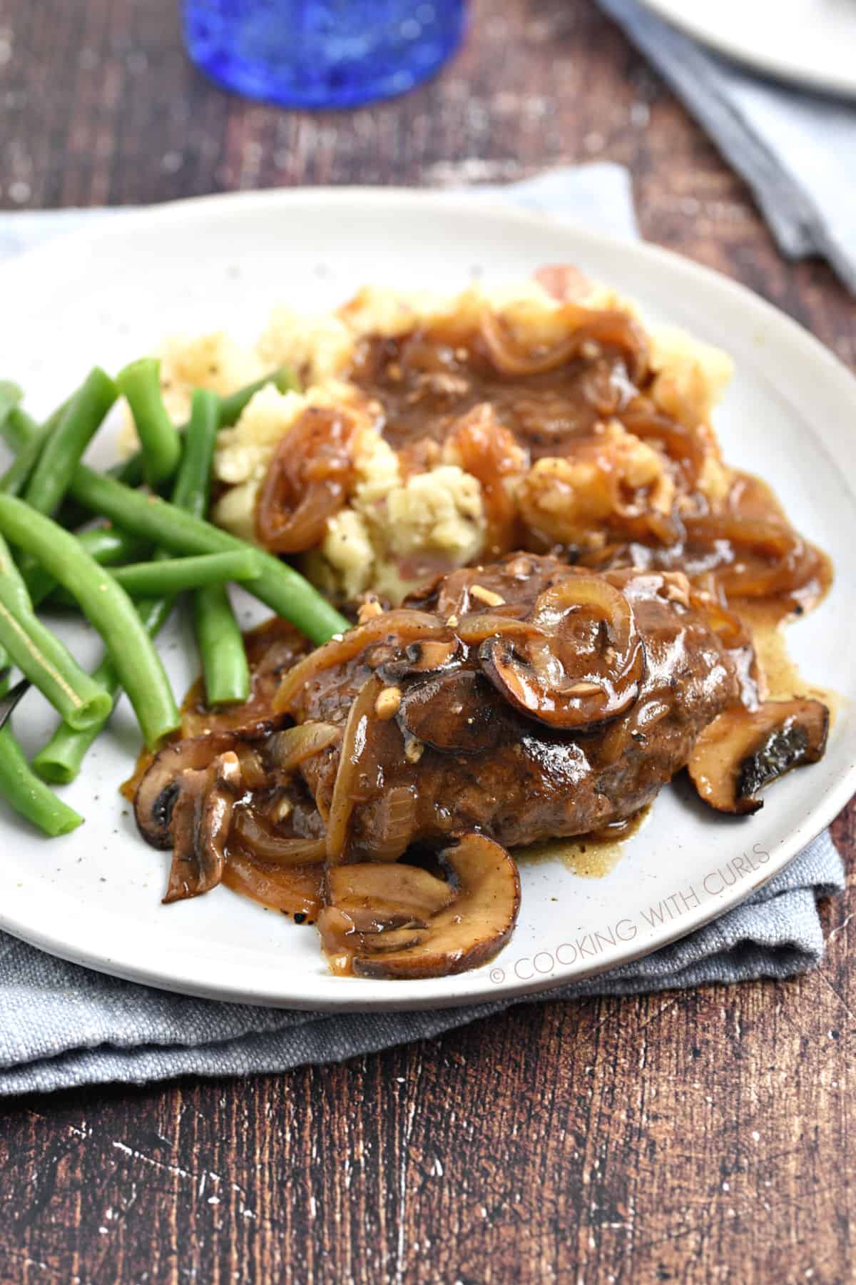 Mushroom gravy topped salisbury steak and mashed potatoes witha  side of green beans.