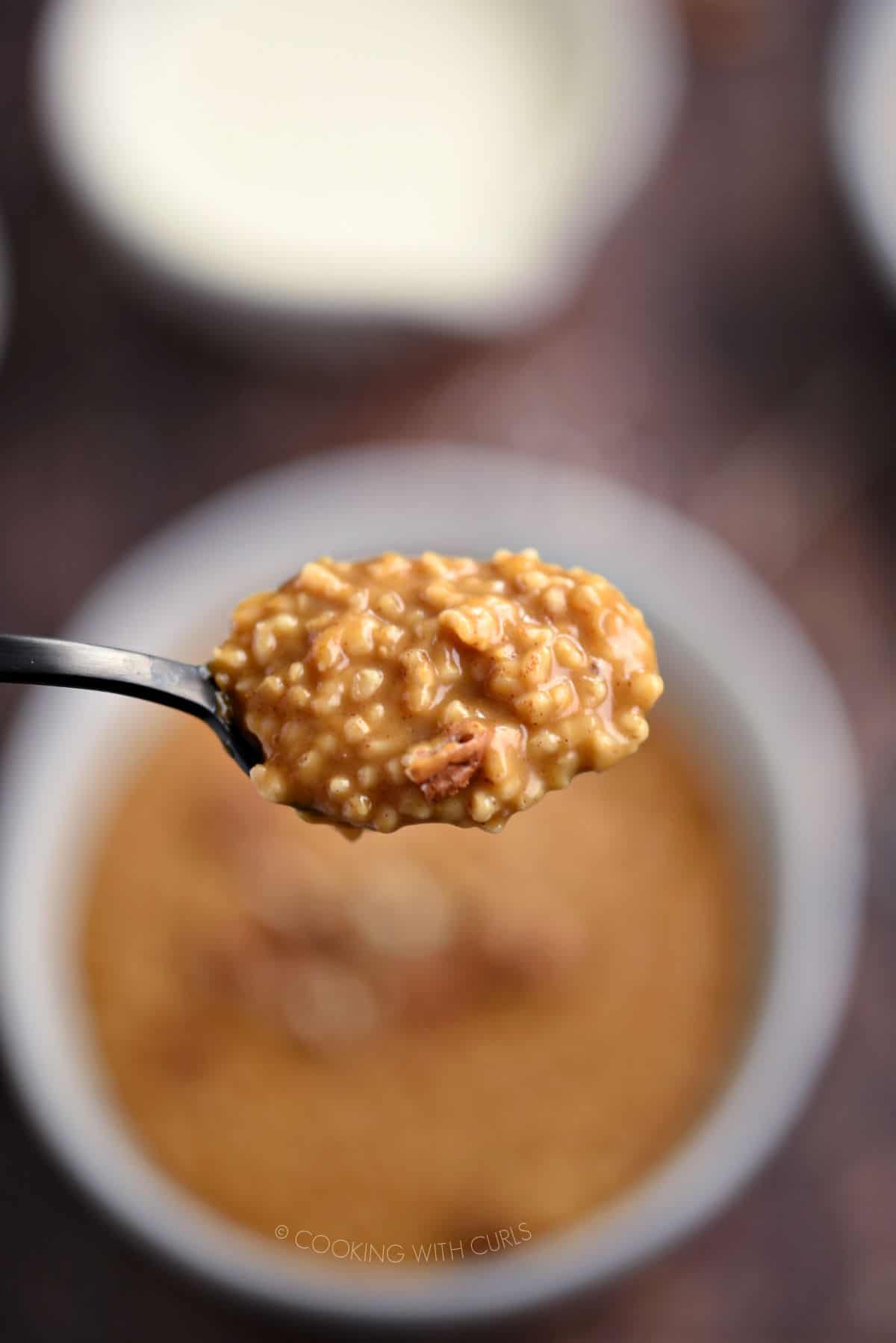 Instant Pot Pumpkin Pie Steel Cut Oatmeal and chopped pecan pieces on a black spoon hovering above a bowl of oatmeal.