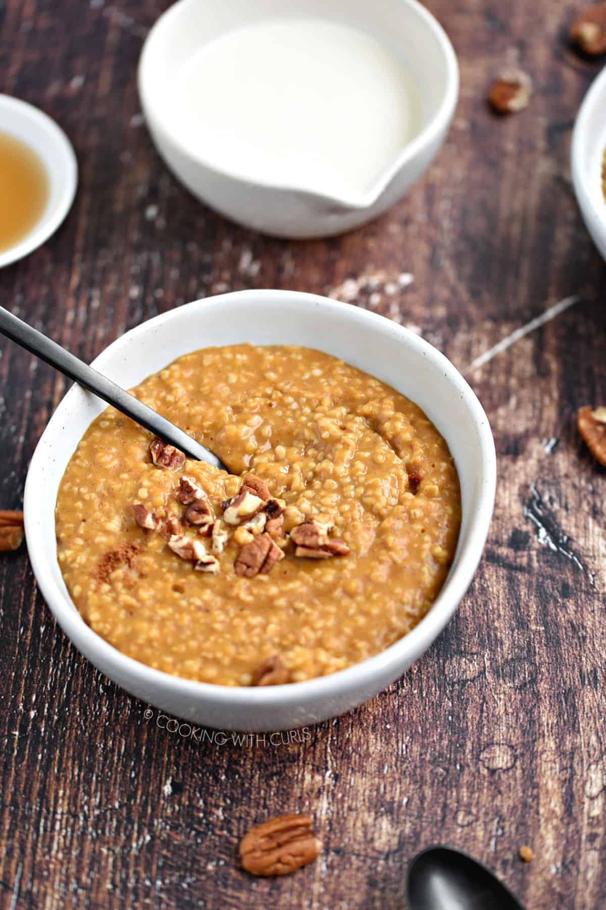 A bowl of pumpkin oatmeal topped with chopped pecans and a black spoon sticking out of the left, upper corner.