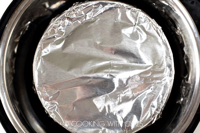 Looking down on a foil wrapped cheesecake inside a pressure cooker.