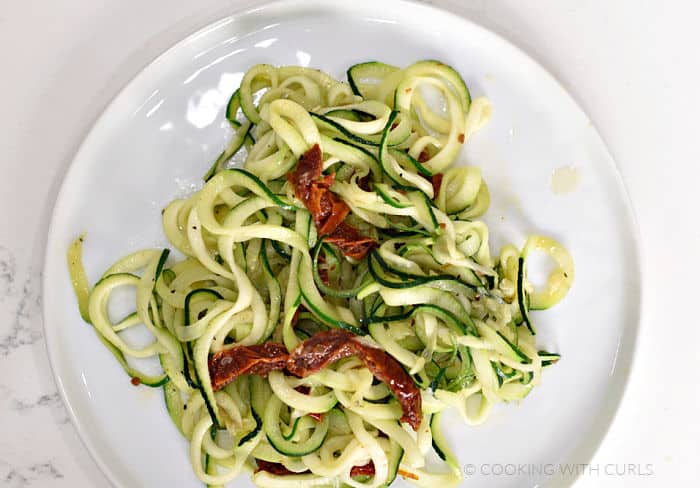 Looking down on a white plate topped with zucchini noodles and tomato strips. 