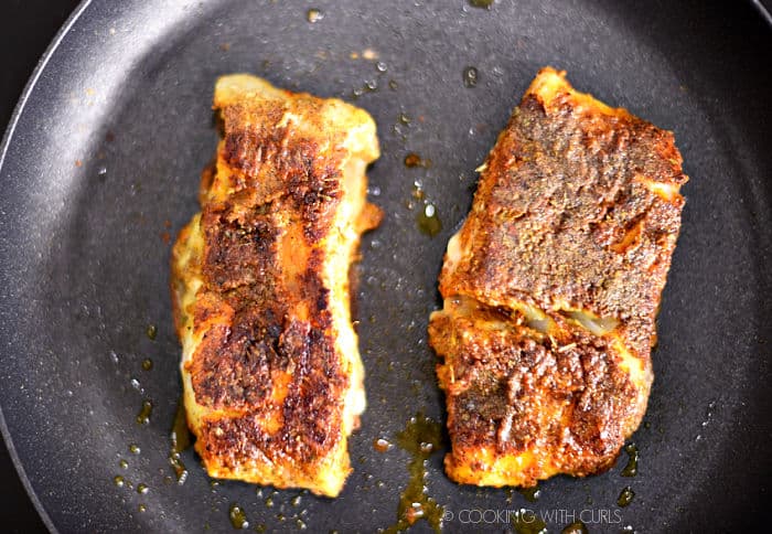 Looking down on two seasoned cod fillets in a non-stick pan. 