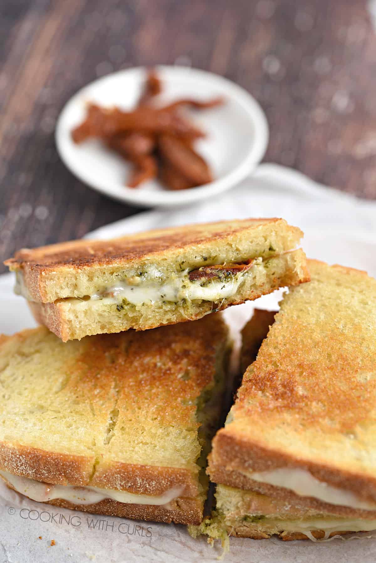 Two pesto grilled cheese sandwiches cut in half and stacked on top of each other, with one side facing the camera.