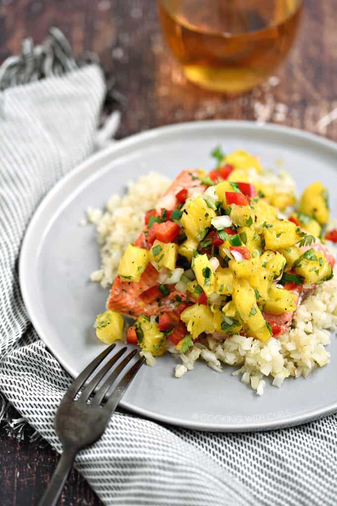 Salmon with Fresh Pineapple Salsa served with cauliflower rice on a gray plate sitting on a white and black striped napkin.