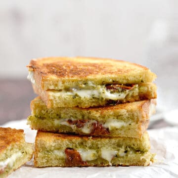 Three pesto grilled cheese halves stacked on top of each other on white parchment paper.