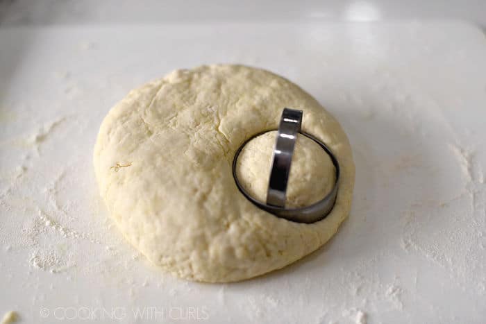 circle cutter in a round ball of dough cutting out a biscuit on a flour covered work surface. 