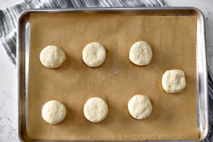 looking down on seven raw biscuits on a parchment lined baking sheet. 