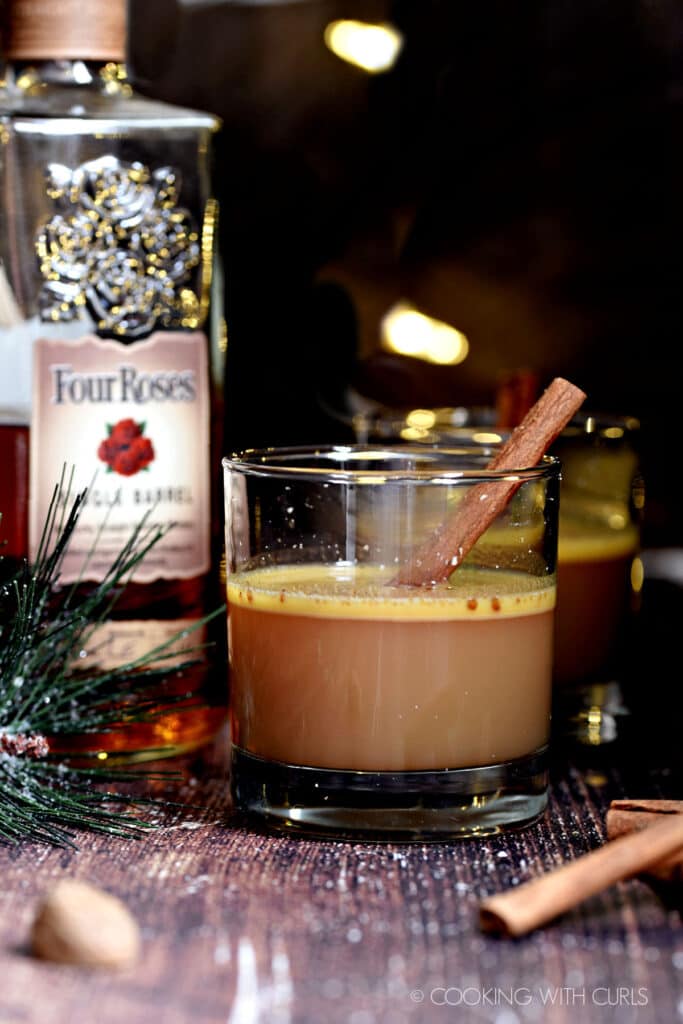 Two glasses with Hot Buttered Bourbon and a cinnamon stick, with a bottle of Four Roses bourbon in the background.