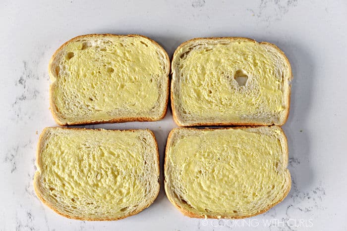 Butter spread on four slices of white bread. 
