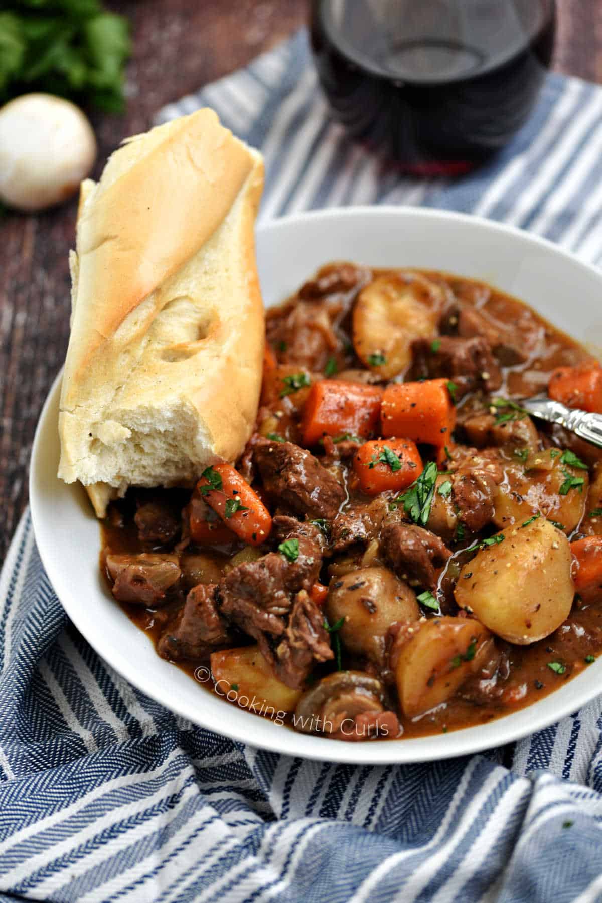 Instant Pot Beef Bourguignon in a bowl with crusty bread and glass of red wine in the background.