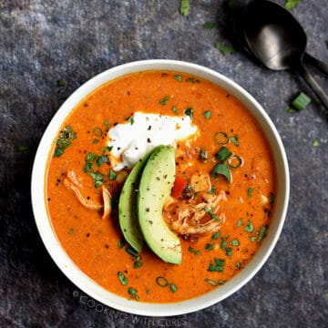 Looking down on a bowl of chicken enchilada soup topped with Greek yogurt, avocado slices and cilantro.
