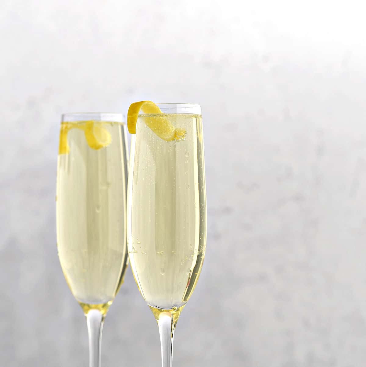 Two champagne flutes filled with Limoncello Spritzer with Prosecco and a lemon twist.