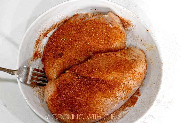 Two chicken breasts covered with taco seasoning in a white bowl. 