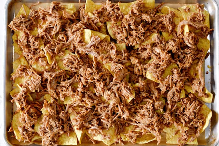 A layer of pulled pork spread over the tortilla chips. 