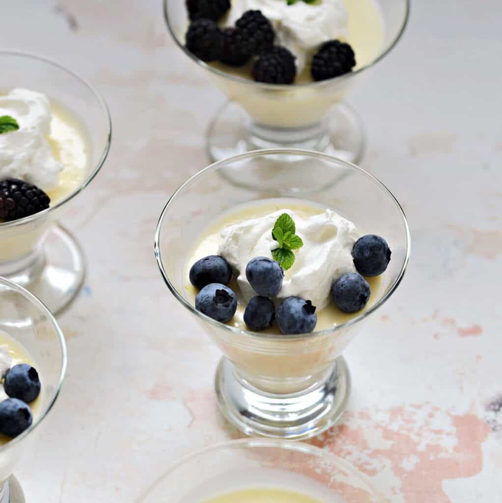 Lemon pudding topped with whipped cream and berries in four glasses.