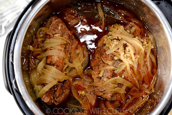 Cooked pulled pork topped with onion slices and garlic  in the pressure cooker liner. 