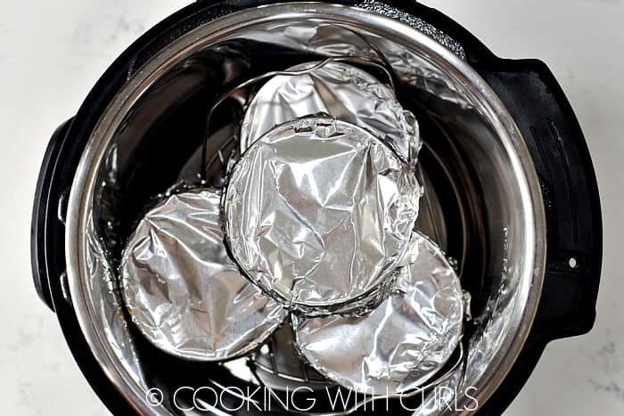 Four foil wrapped ramekins stacked in a pressure cooker. Three on the bottom and one on top.