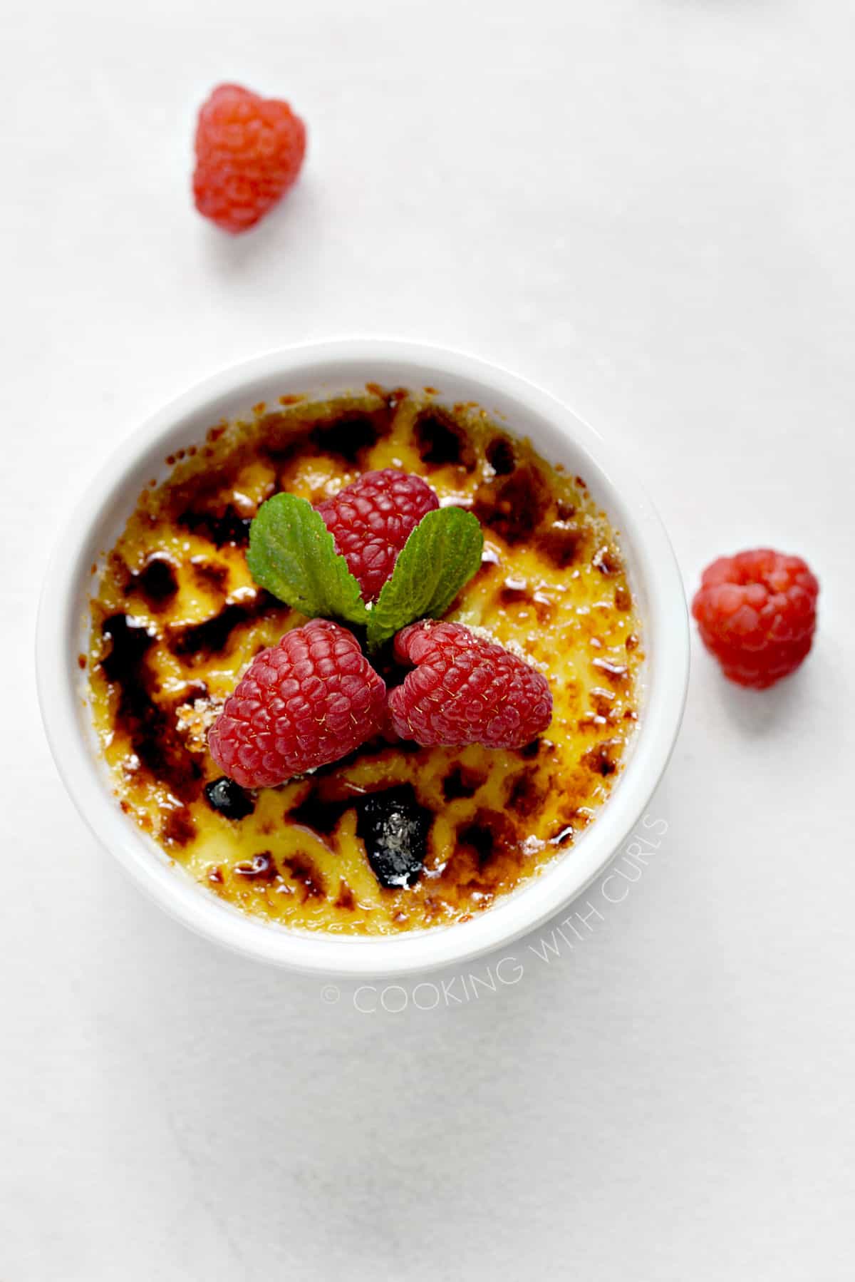 Instant Pot Creme Brulee in a white ramekin, topped with fresh raspberries. 