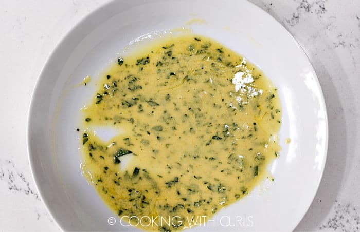 Mustard, lemon juice, parsley and butter mixed together on a white plate.