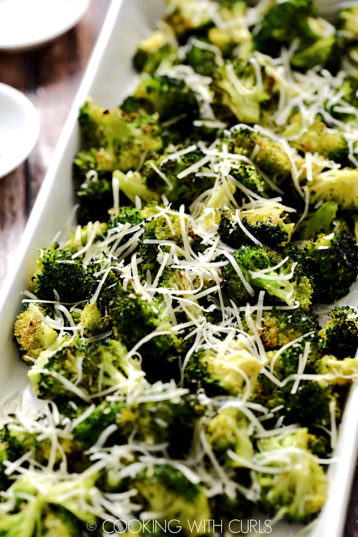 Oven Roasted Broccoli in a white, rectangle platter topped with grated Parmesan. 