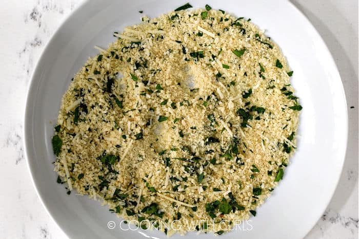 Panko, parsley and Parmesan mixed together on a white plate. 