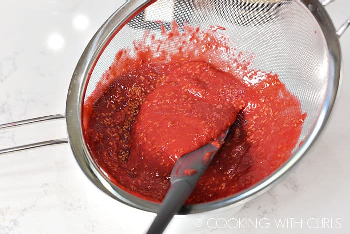 Raspberry puree in a fine mesh strainer with a rubber spatula to push it through. 