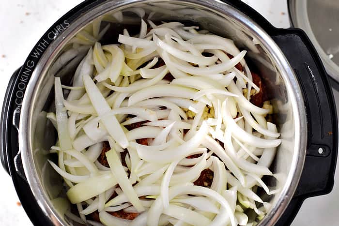 Sliced onions laying on top of the pork pieces in the pressure cooker. 