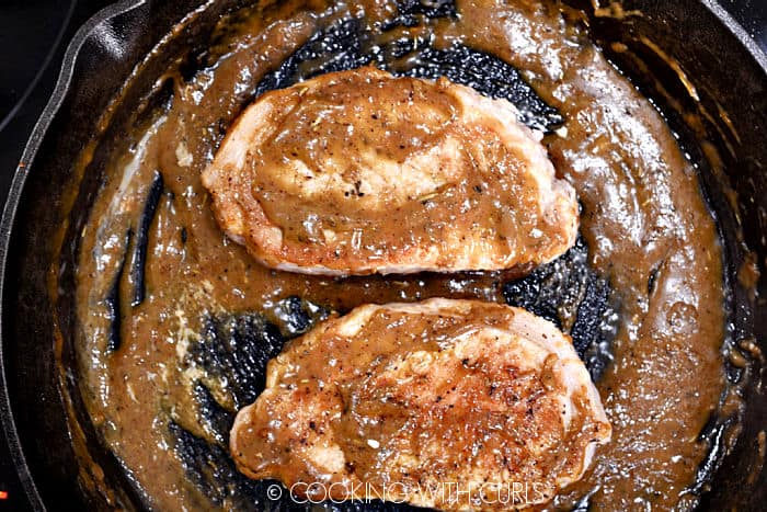 Two pork chops coated with pan gravy in a cast iron skillet. 