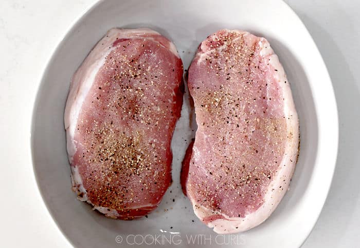 Two pork chops with salt and pepper sitting in a white bowl. 