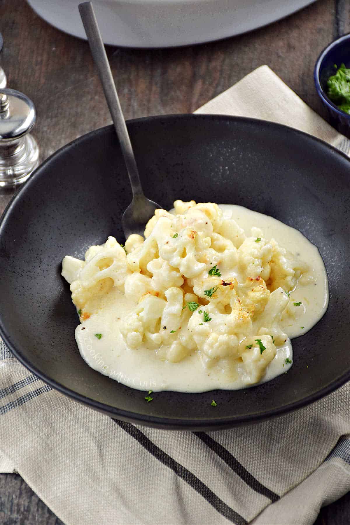 Cauliflower pieces topped with a creamy cheese sauce in a bowl with a fork poking in on the right side.