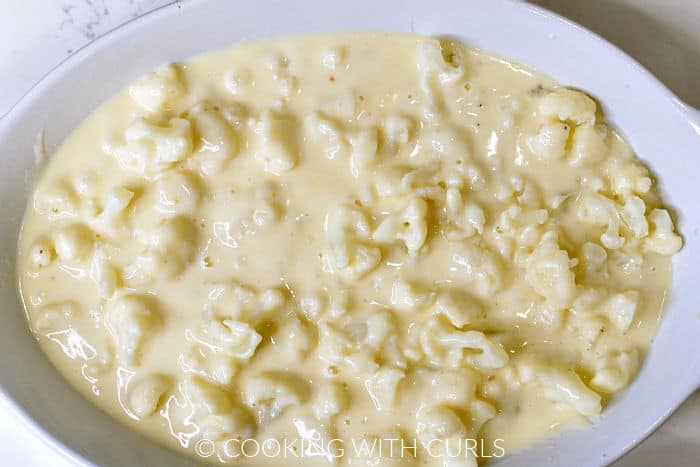 Cheese sauce poured over the steamed cauliflower in a white baking dish. 