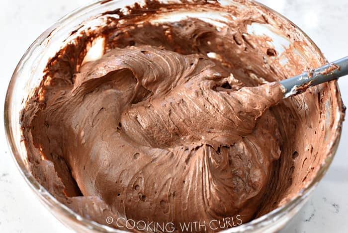 Chocolate cheesecake mixture mixed together in a glass bowl with a silicone spatula. 