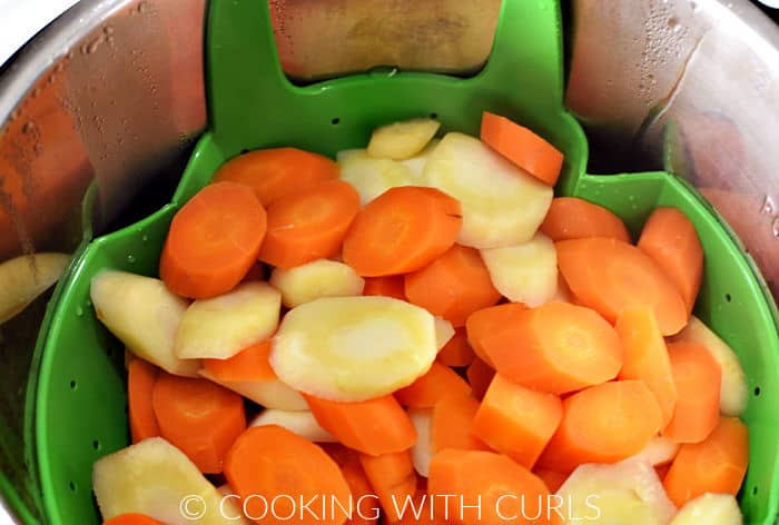 Cooked carrots and parsnips in a green strainer inside a pressure cooker. 