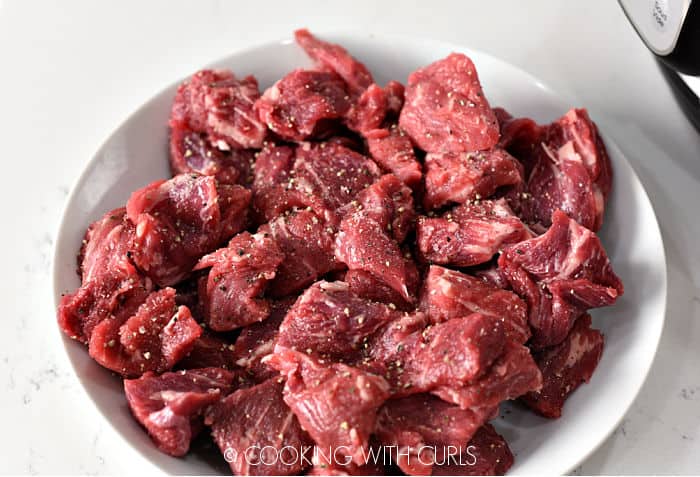 Cubed chuck roast tossed with salt and pepper in a white bowl. 