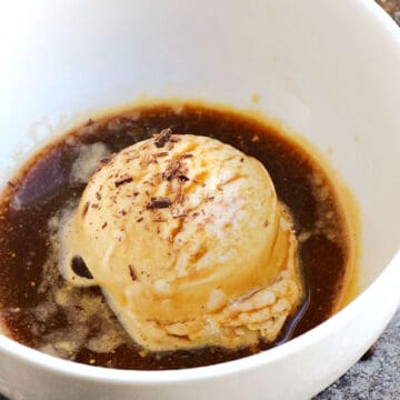A scoop of ice cream in a white bowl topped with espresso and chocolate shavings.
