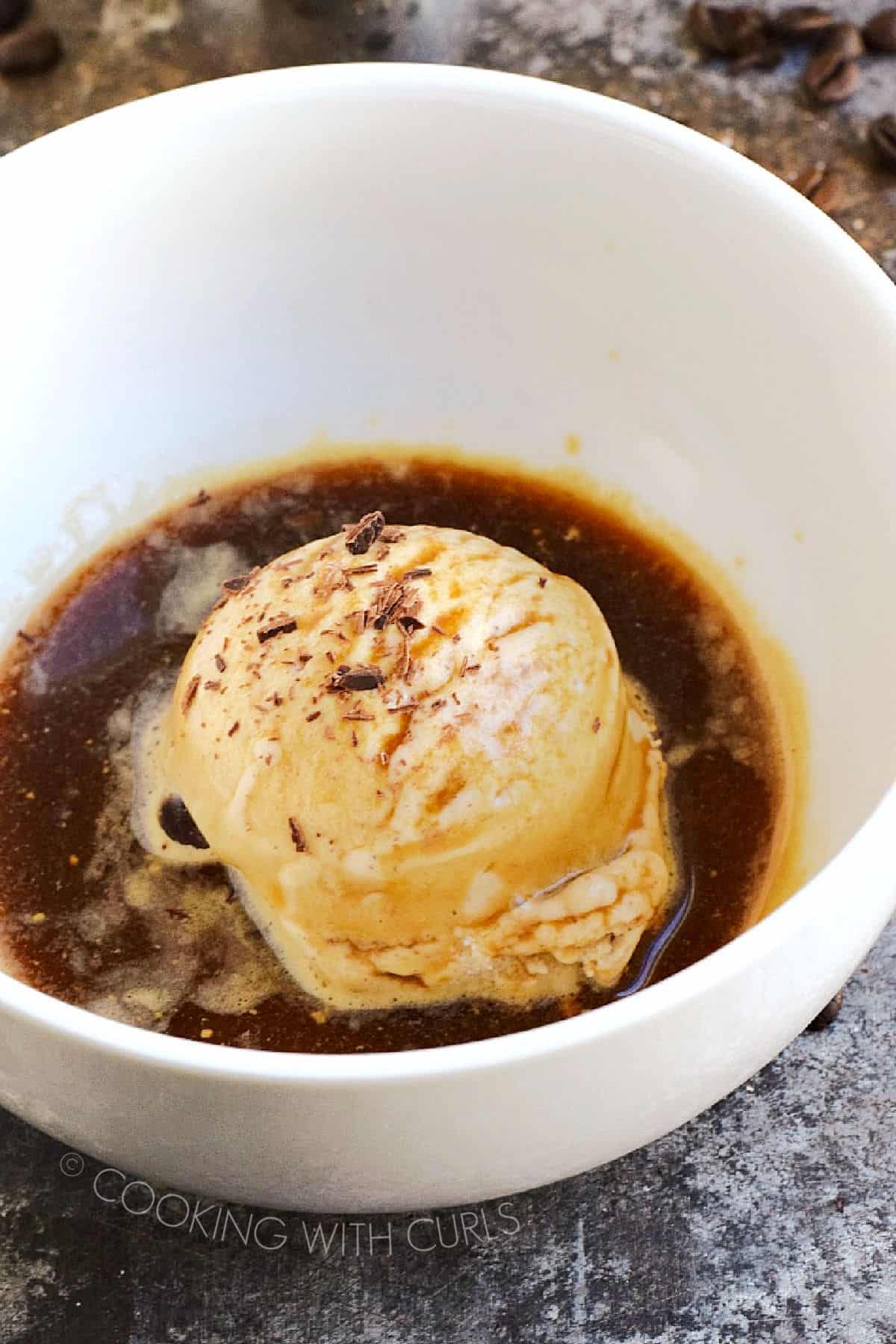 A scoop of ice cream topped with espresso and chocolate shavings in a white bowl.