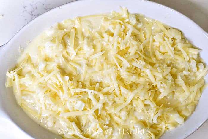 Grated cheese on top of the cauliflower and sauce mixture in a white baking dish. 