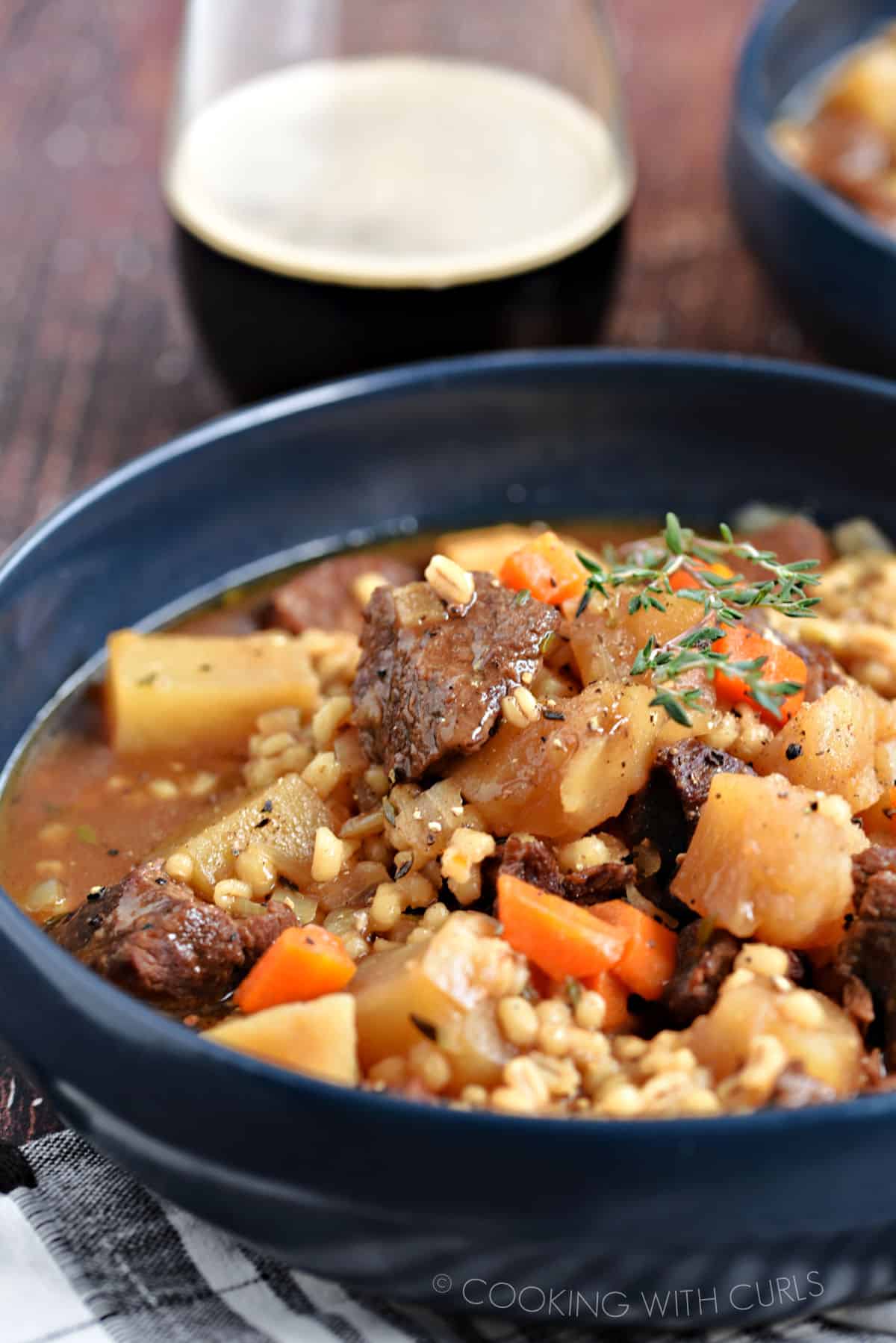 Large chunks of beef, potatoes and carrots surrounded by barley and broth in a blue bowl.