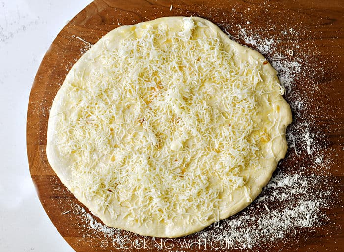Lemon-garlic sauce and grated cheese sprinkled over the pizza circle on a wooden pizza peel. 