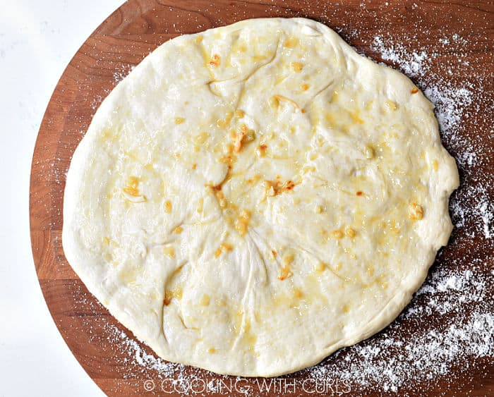 Lemon-garlic sauce brushed onto the top of a pizza dough circle on a wooden pizza peel. 